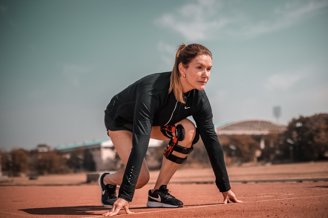 Athlete recovery with a knee massager — a woman crouches down to pick up a tennis ball
